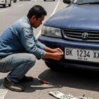 GANTI PLAT - Ilustrasi seseorang menggantilan plat kendaraannya di pinggir jalan. Gambar ini dibuat dengan AI Gemini pada Minggu (5/10/2025)