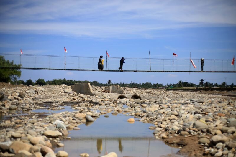 Warga korban bencana Banjir saat melintasi jembatan gantung  garuda yang baru selesai di bangun pasca bencana banjir di Dese Seunong, kecamatan Meurah Dua, kabupaten Pidie Jaya, Jumat (16/1/2026).(Foto : Farid Ismullah/NOA.co.id).