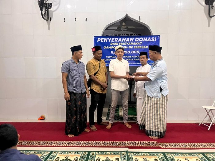 Keuchik Leu Ue Yusri menyerahkan donasi sebesar Rp10,9 juta kepada Muhammad Israk Siregar sebagai ahli waris, di Meunasah Gampong Leu Ue, Jumat malam (23/1/2026). Foto: Dok. MC Aceh Besar