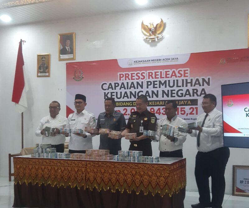 Kajari Aceh Jaya Badri Wasil (berbaju dinas) bersama unsur Pemerintah Kabupaten Aceh Jaya, Ketua Dprk dan pihak Bank Aceh memperlihatkan uang hasil pemulihan keuangan negara saat konferensi pers di Aula Kejari Aceh Jaya, Calang, Selasa (22/7/2026). Foto: Dok. Sanusi/NOA.co.id