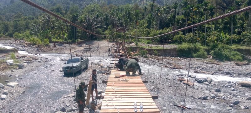 Personel Babinsa Posramil Lawe Sumur bersama teknisi lapangan dan masyarakat bergotong royong memasang papan lantai Jembatan Gantung Perintis di Desa Teger Miko, Kecamatan Lawe Sumur, Aceh Tenggara, Senin (6/7/2026). Foto: Dok. Istimewa 