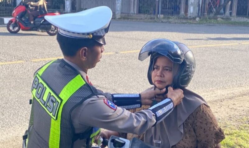 Personil Satlantas Polres Abdya memakai helm kepada salah seorang pengguna jalan raya. Foto. Dok. Teukunizar/noa.co.id