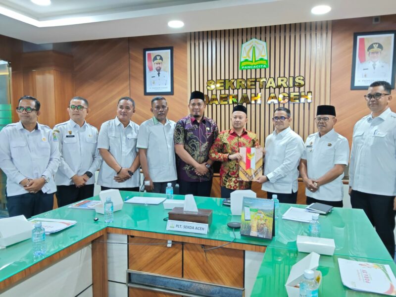 Bupati Aceh Jaya, Safwandi berbaju batik kuning merah, menyerahkan berkas kepada Plt Sekda Aceh, Taufik, dalam rapat persiapan PORA XV/2026, di ruang rapat Sekretaris Daerah Aceh, Rabu (7/10/2026). Foto: Dok. Pemkab Aceh Jaya