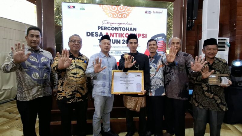 Bupati Aceh Jaya, Safwandi, (baju putih bermotif kotak-kotak dan peci hitam), bersama jajaran pejabat dan perwakilan Gampong Kabong saat menerima penghargaan Desa Percontohan Antikorupsi dari KPK RI di Banda Aceh, Rabu (21/10/2026). Foto: Dok. DPMPKB Aceh Jaya
