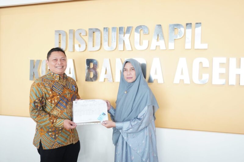 Kepala Disdukcapil Kota Banda Aceh, Heru Triwijanarko menyerahkan KK dan KTP kepada Mardalena dengan status pekerjaan sebagai pensiunan di Kantor Disdukcapil Kota Banda Aceh, Kamis (29/10/2026). Foto: Dok. Diskominfo Kota Banda Aceh