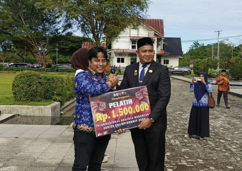 Sekda Aceh Jaya, H. Masri, menyerahkan bonus kepada pelatih taekwondo Aceh Jaya atas prestasi yang diraih dalam ajang Internasional Kesatria Nusantara PBTI Series Championship 2026, di halaman Kantor Bupati Aceh Jaya, Rabu (28/10/2026). Foto: Dok. Pemkab Aceh Jaya